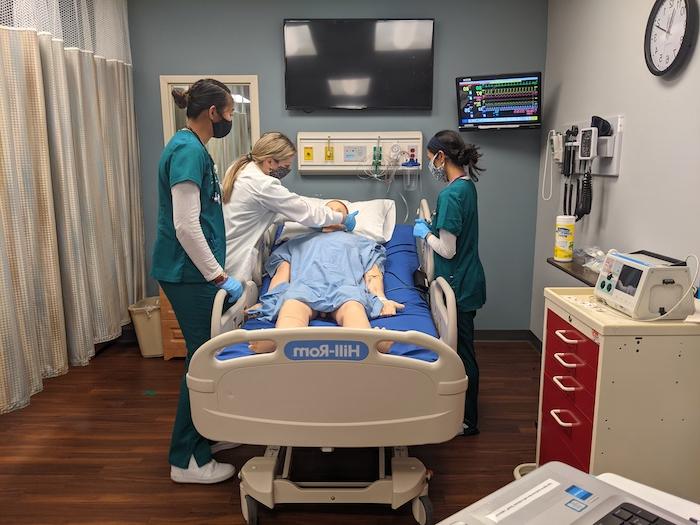 Three nursing student practicing on a model patient in a simulation center.